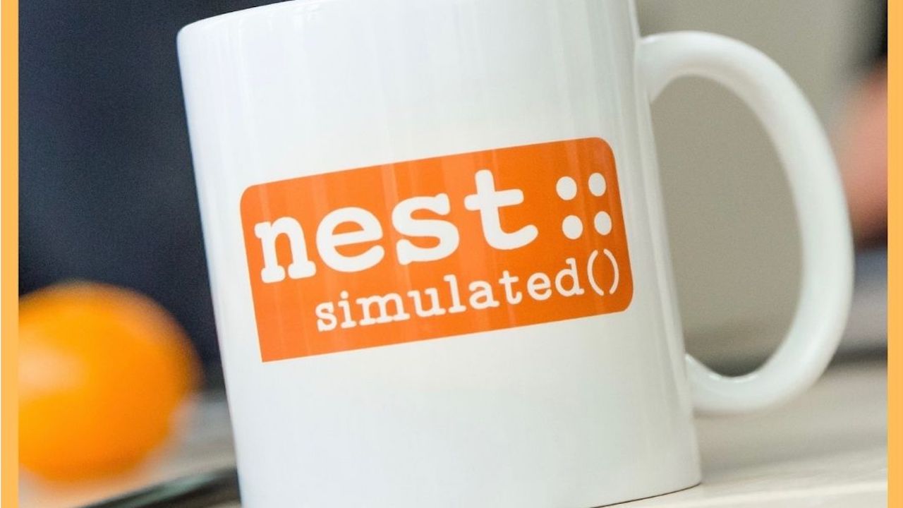 A white coffee cup with the orange “nest::simulated()” logo.
