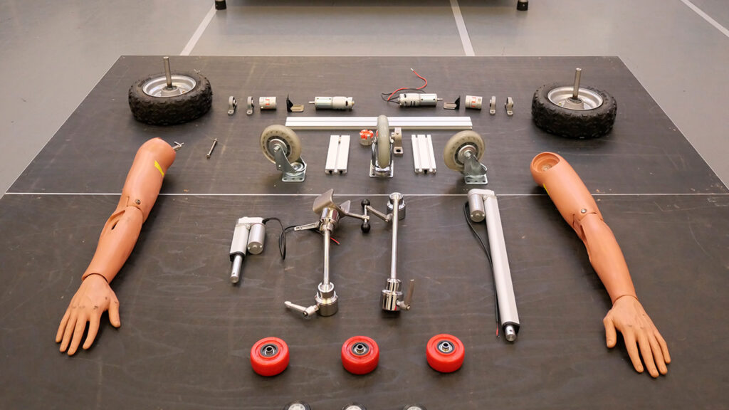 Various metal and plastic robot pieces on a table, including wheels and a pair of prosthetic arms.