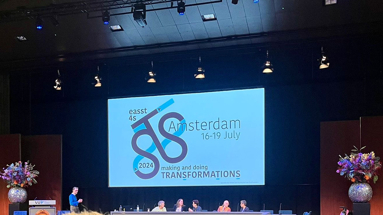 Conference panel on stage with a large screen showing logo, name and date of the conference.