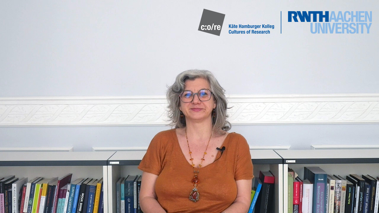 Woman wearing orange t-shirt and glasses, sitting in front of a bookshelf.
