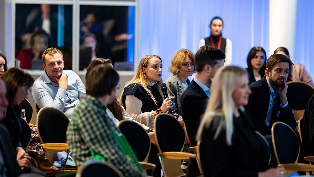 Audience seated in rows of chairs, one holding a microphone.