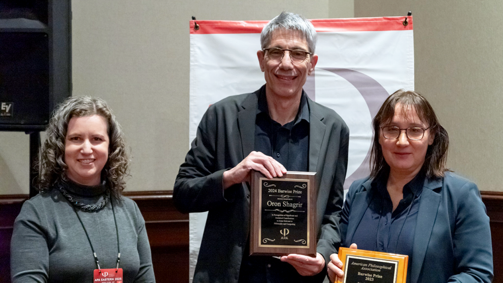 Three people posing, two of them holding an award plaque.