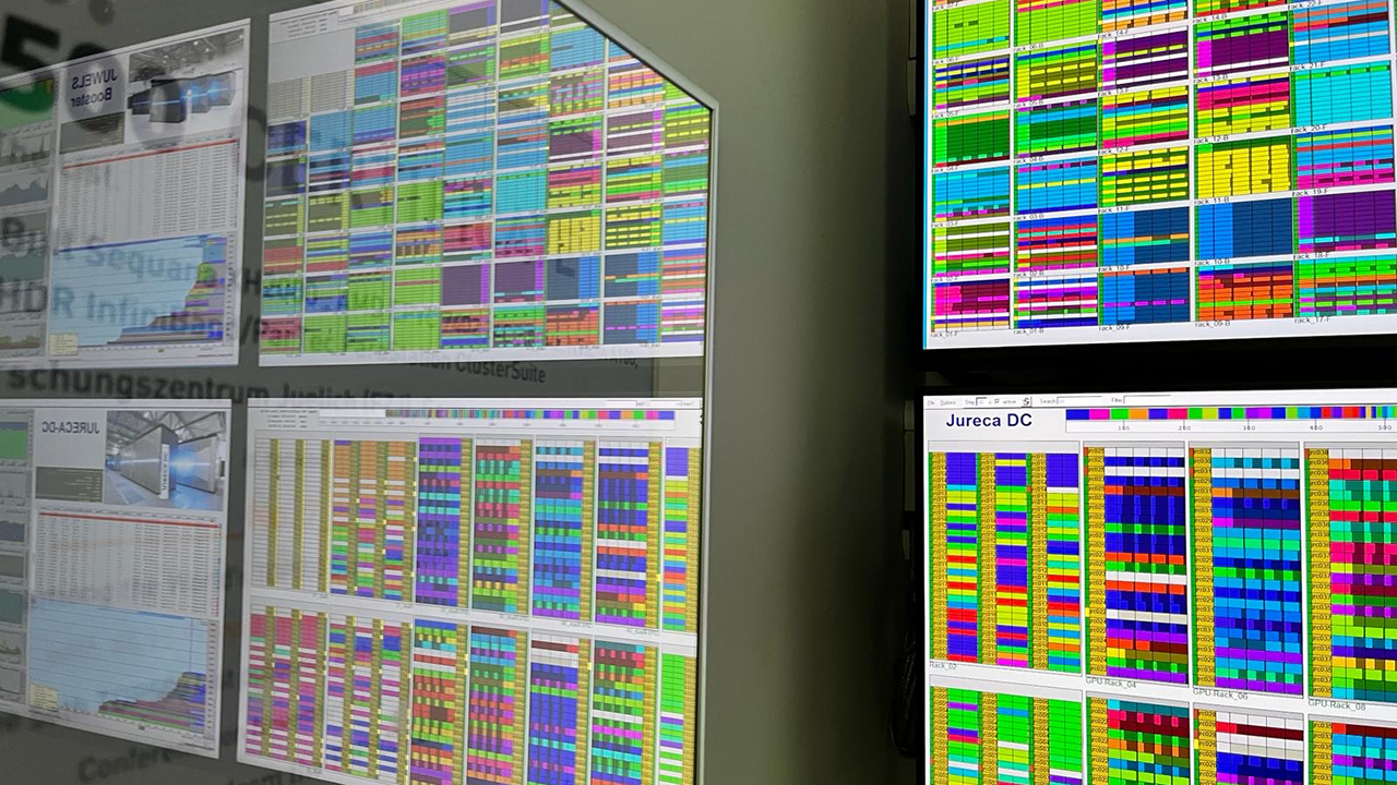 Wall of computer monitors displaying colorful data visualizations and workload schedules from a high-performance computing system.