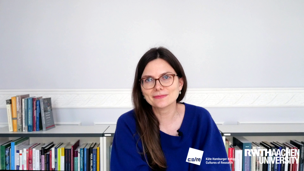 Woman in blue blouse sitting in front of a bookshelf.
