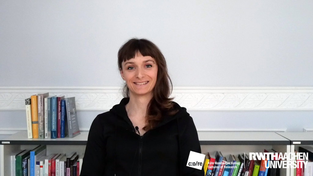 A female person in black smiling and sitting in front of a bookshelf.