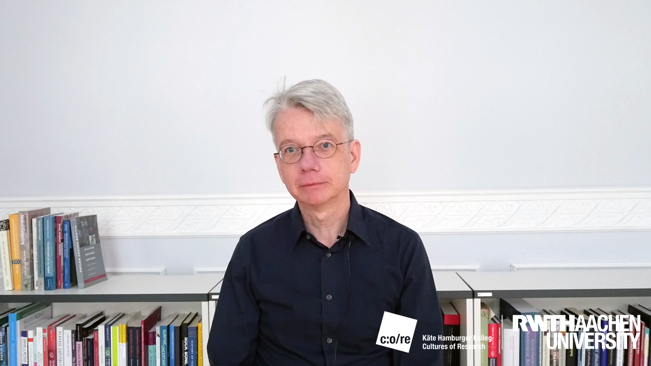 Man in black shirt sitting in front of a bookshelf.