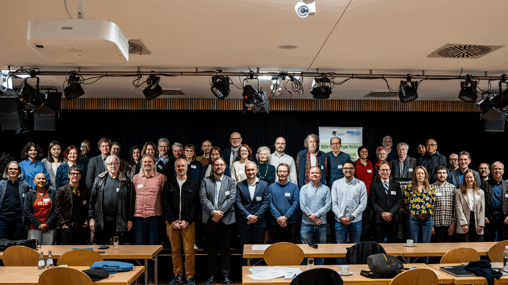 Group photo with 40+ people posing formally in a lecture hall.