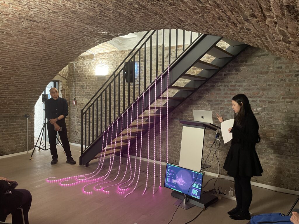 IMG_1425 Two people presenting an art installation with a monitor and pink light tubes hanging on stairwell.